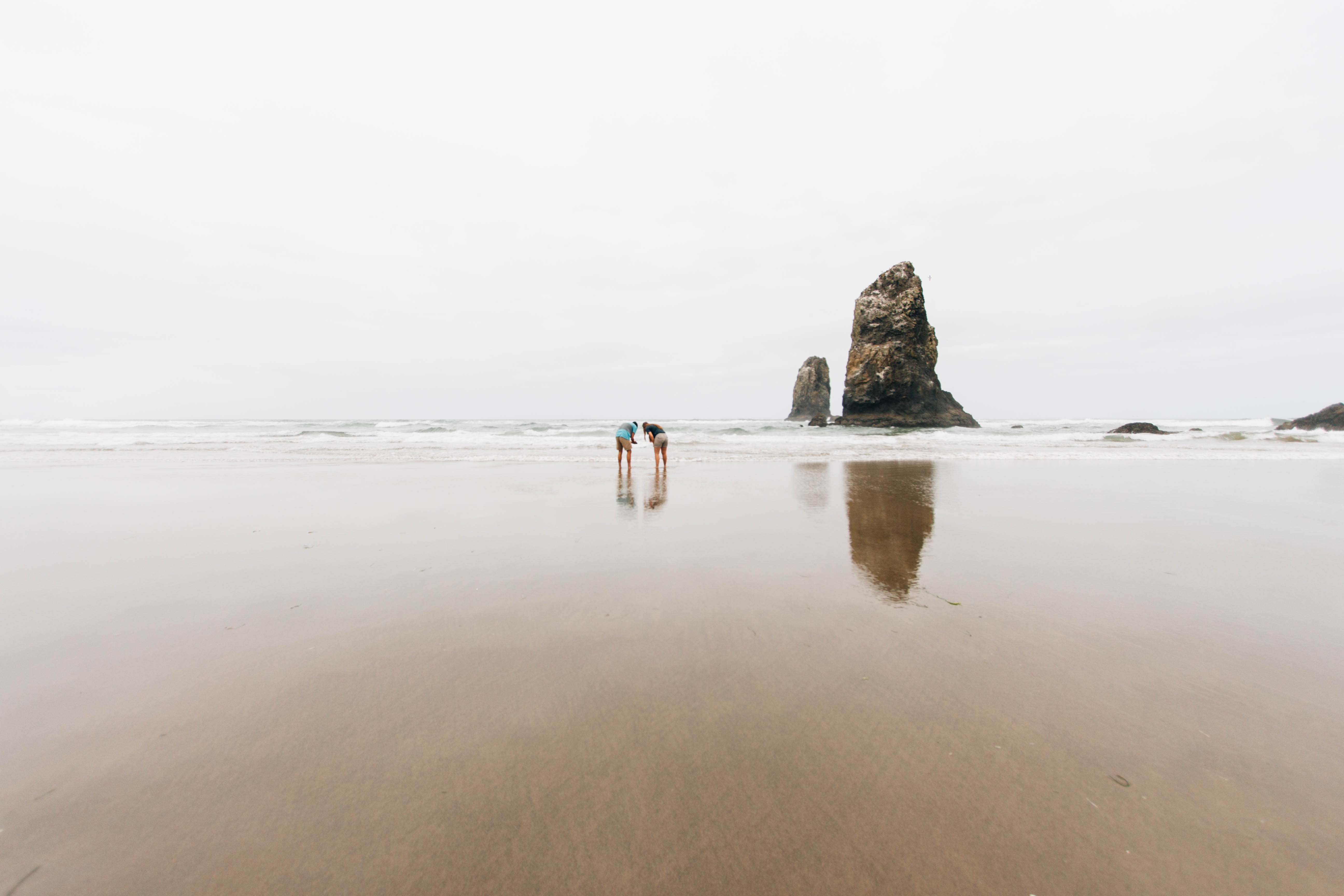 two person on seashore near brown rock formation under white sky during daytime
