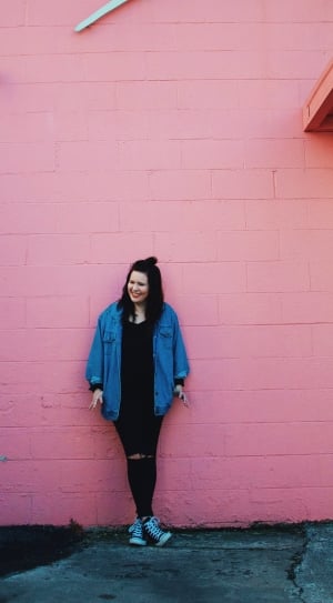 woman in blue button-up long sleeve jacket leaning on pink surface thumbnail