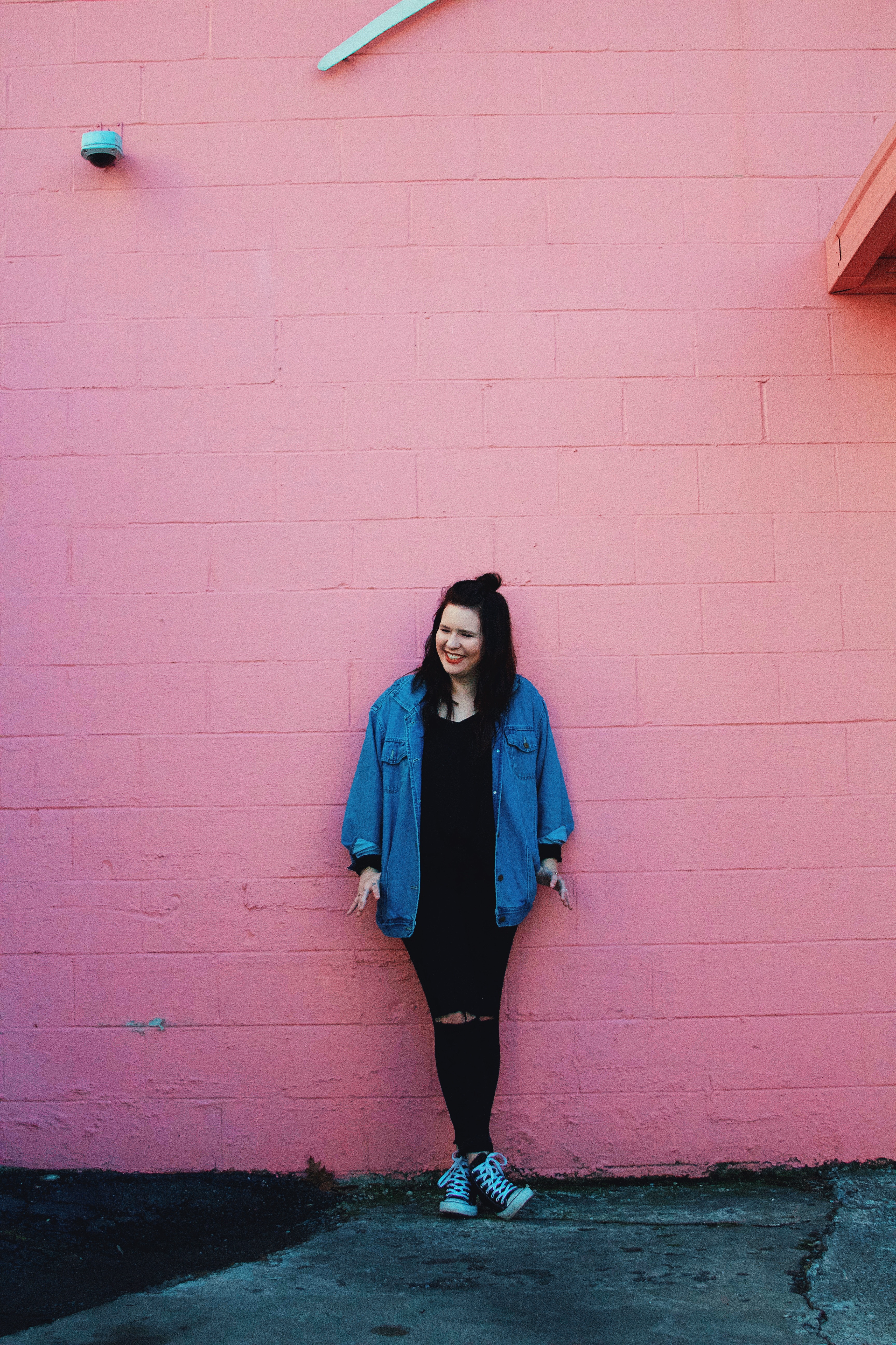 woman in blue button-up long sleeve jacket leaning on pink surface