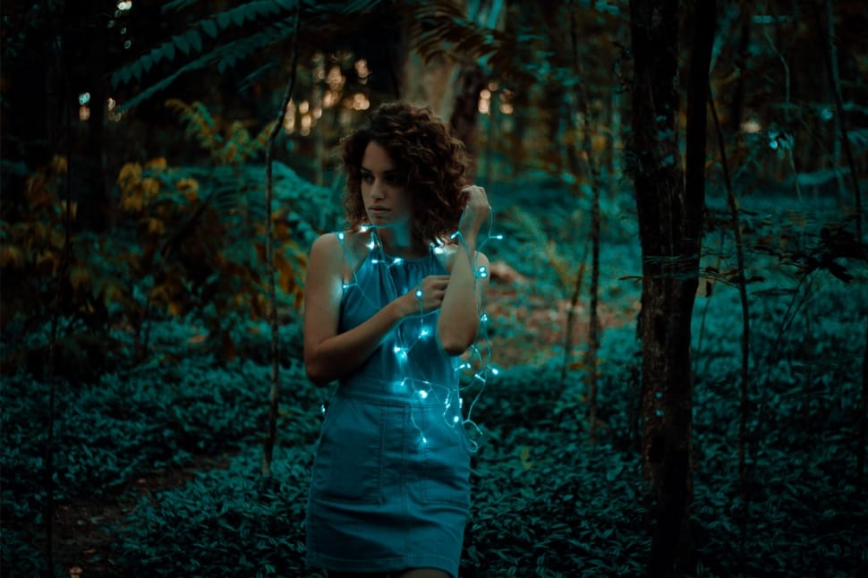 woman standing near forest with string lights on body preview