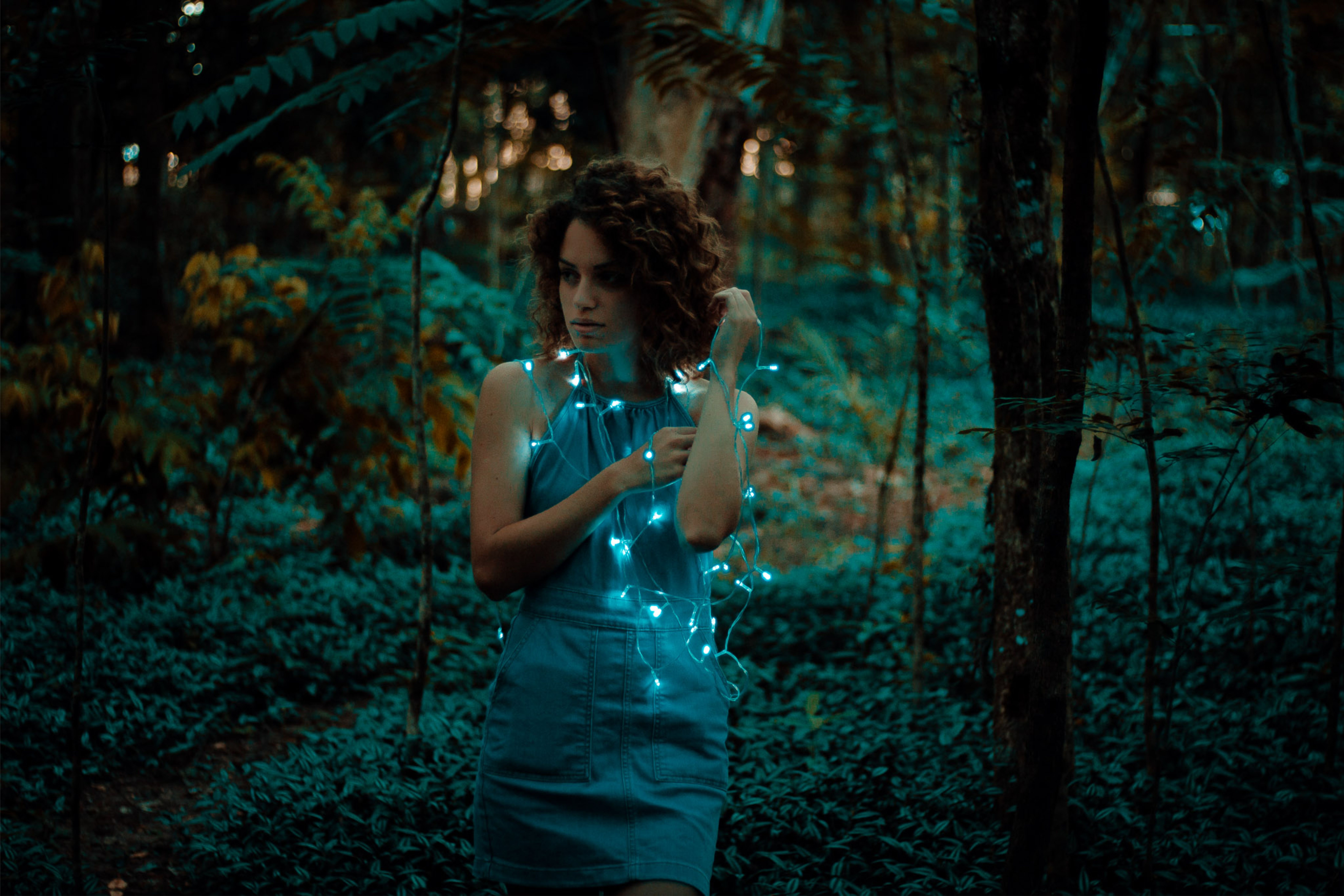 woman standing near forest with string lights on body
