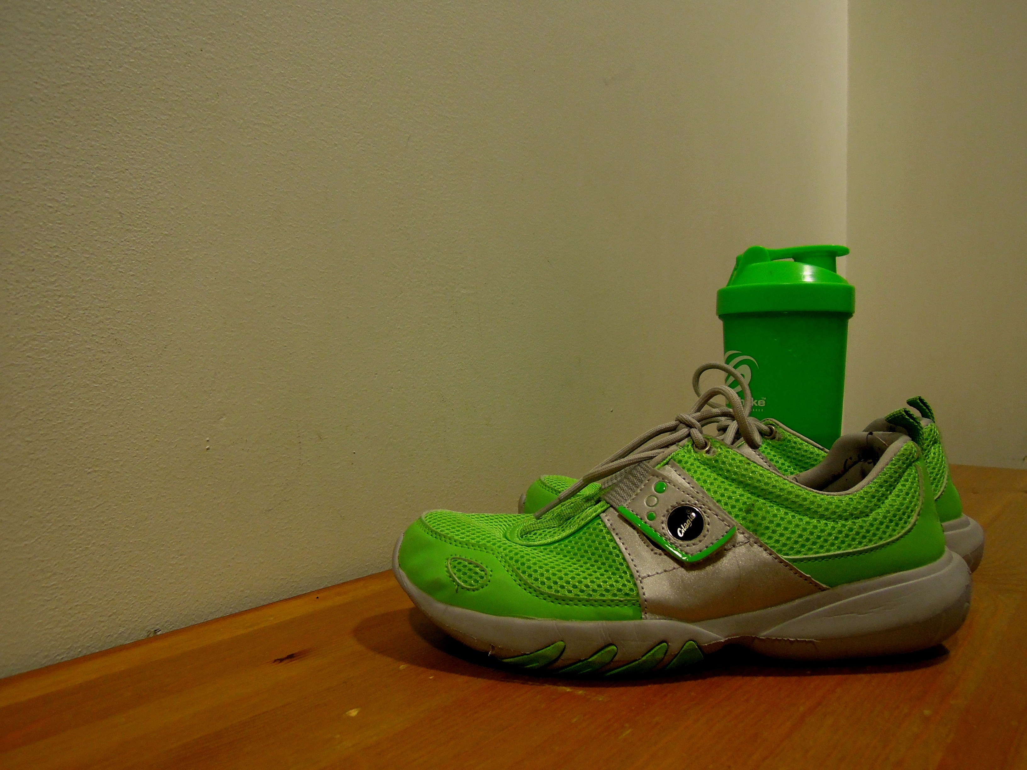 pair of green-and-gray running shoes on brown wooden flooring
