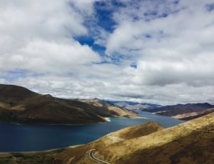 aerial view of brown mountains and body of water under cloudy sky thumbnail