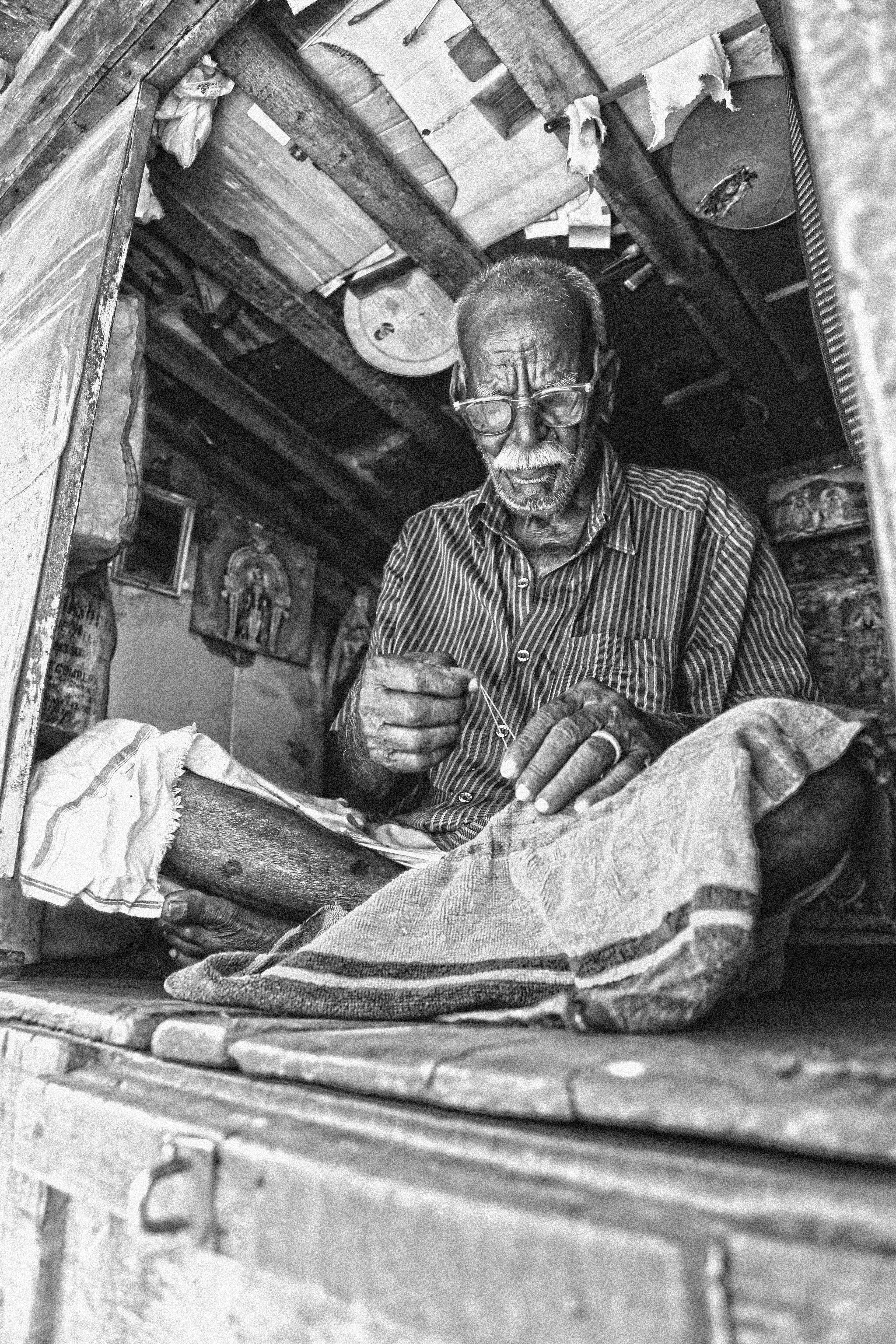 grayscale photography of man wearing eyeglasses while sewing clothe