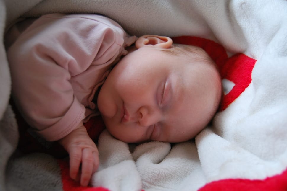 baby in pink long sleeve shirt sleeping white and red bed preview