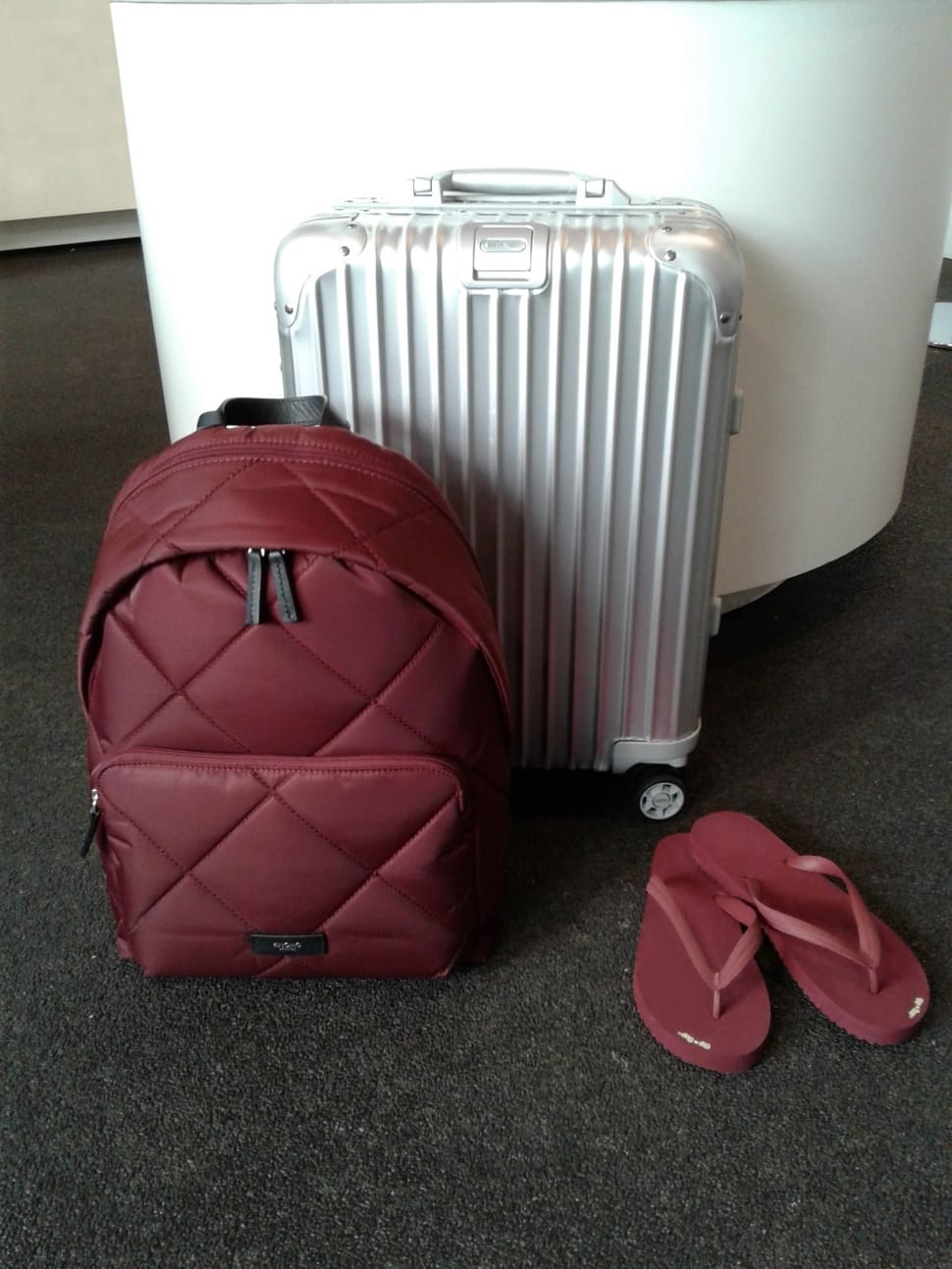 red backpack pair of red flip flops and silver luggage bag preview
