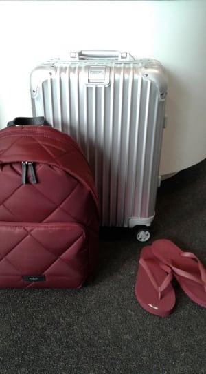red backpack pair of red flip flops and silver luggage bag thumbnail