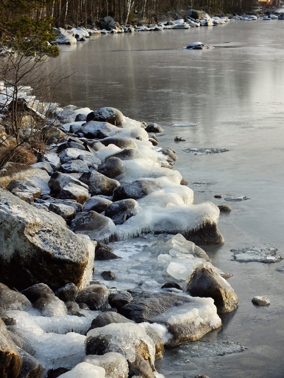 brown rocks beside body of water with snow during daytime preview