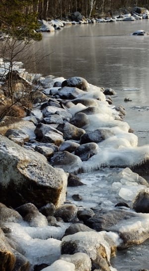 brown rocks beside body of water with snow during daytime thumbnail