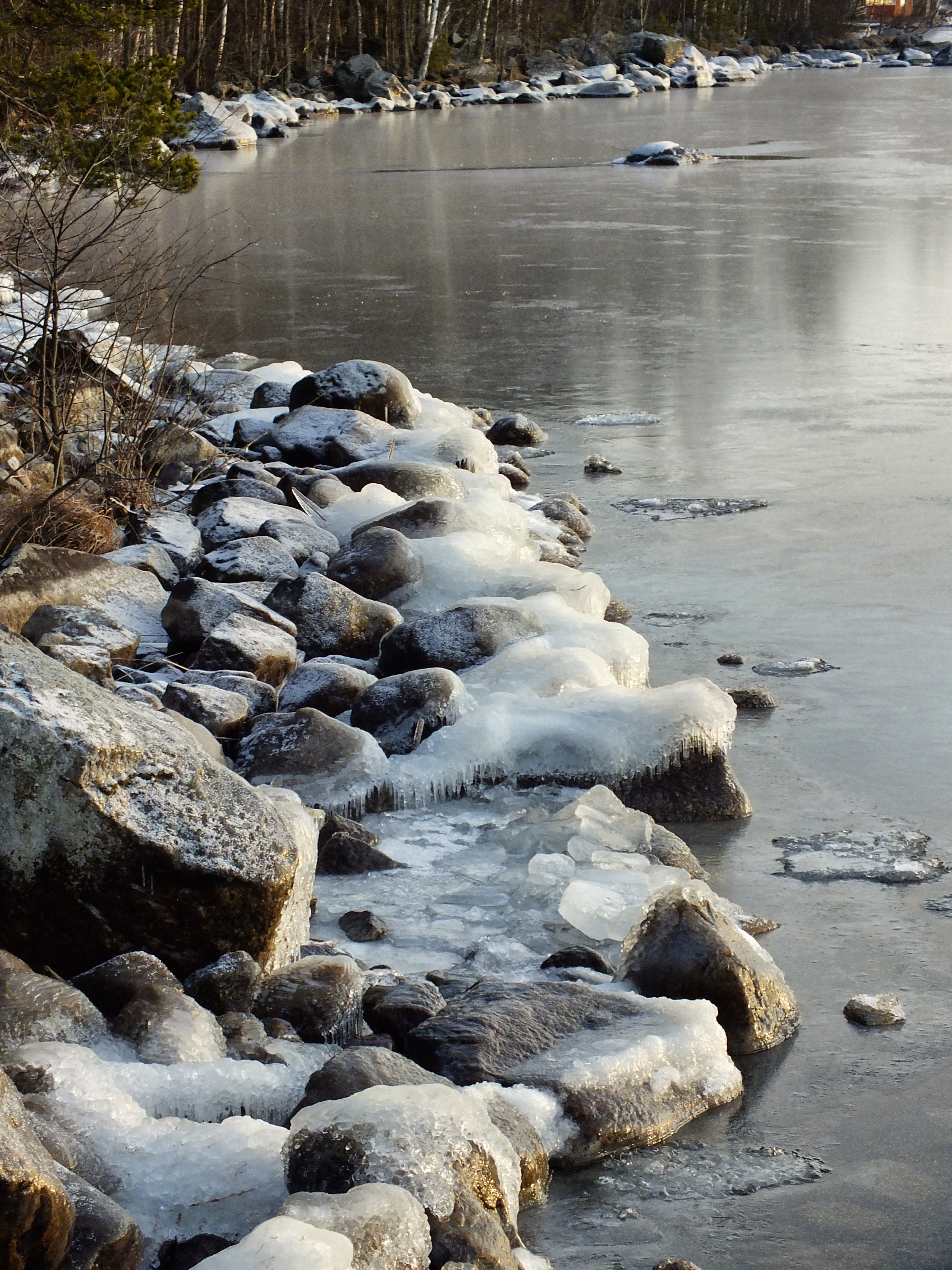 brown rocks beside body of water with snow during daytime