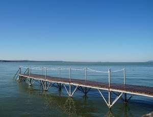 brown wooden boardwalk on calm body of water under blue calm sky thumbnail