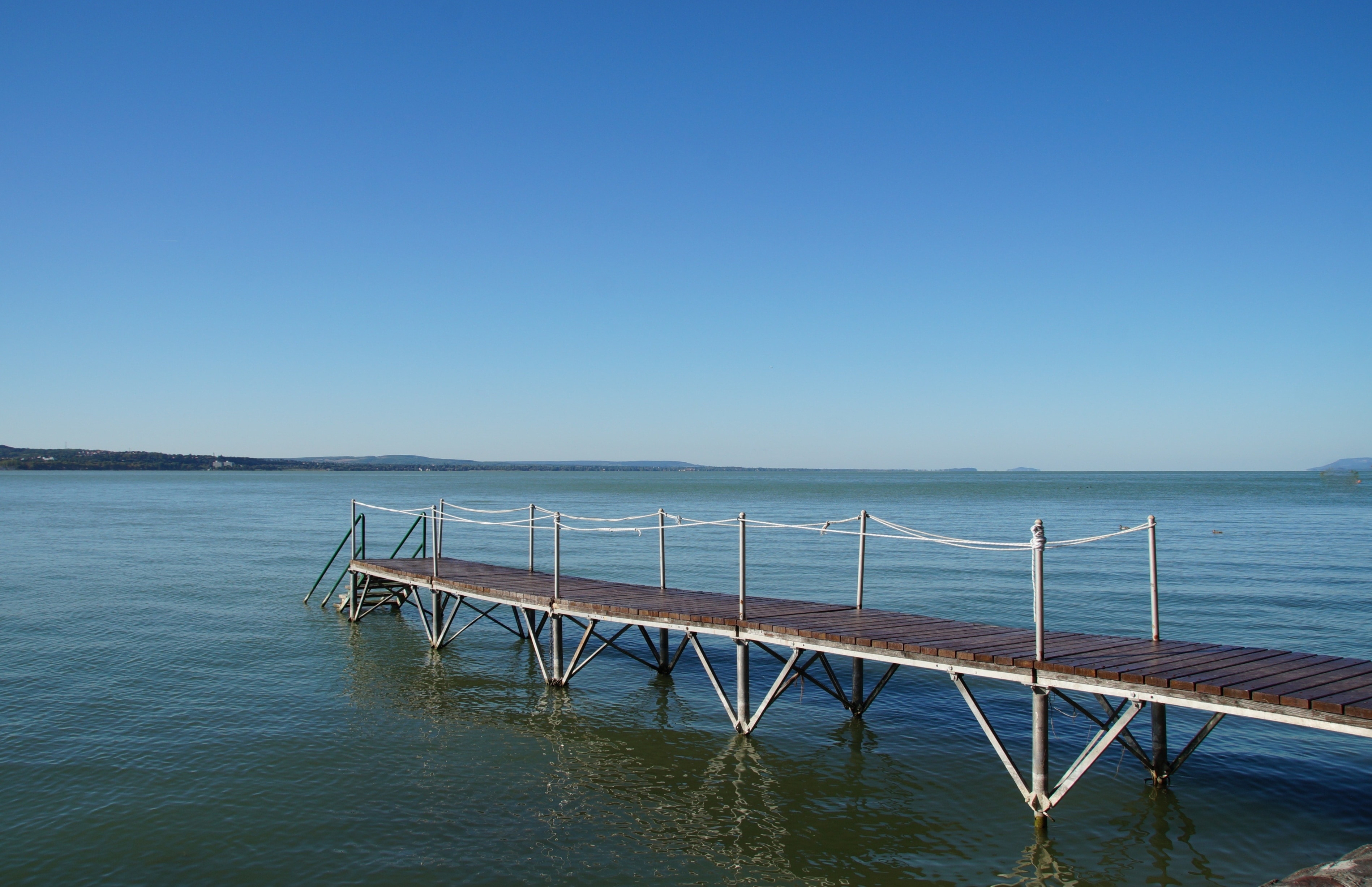 brown wooden boardwalk on calm body of water under blue calm sky
