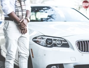 man in white jacket; burberry scarf; gold round bezel watch; and white jeans standing besides white bmw m series sedan parked on road during daytime thumbnail