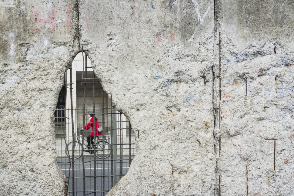 black haired female riding on bicycle seen through hole in gray concrete wall preview