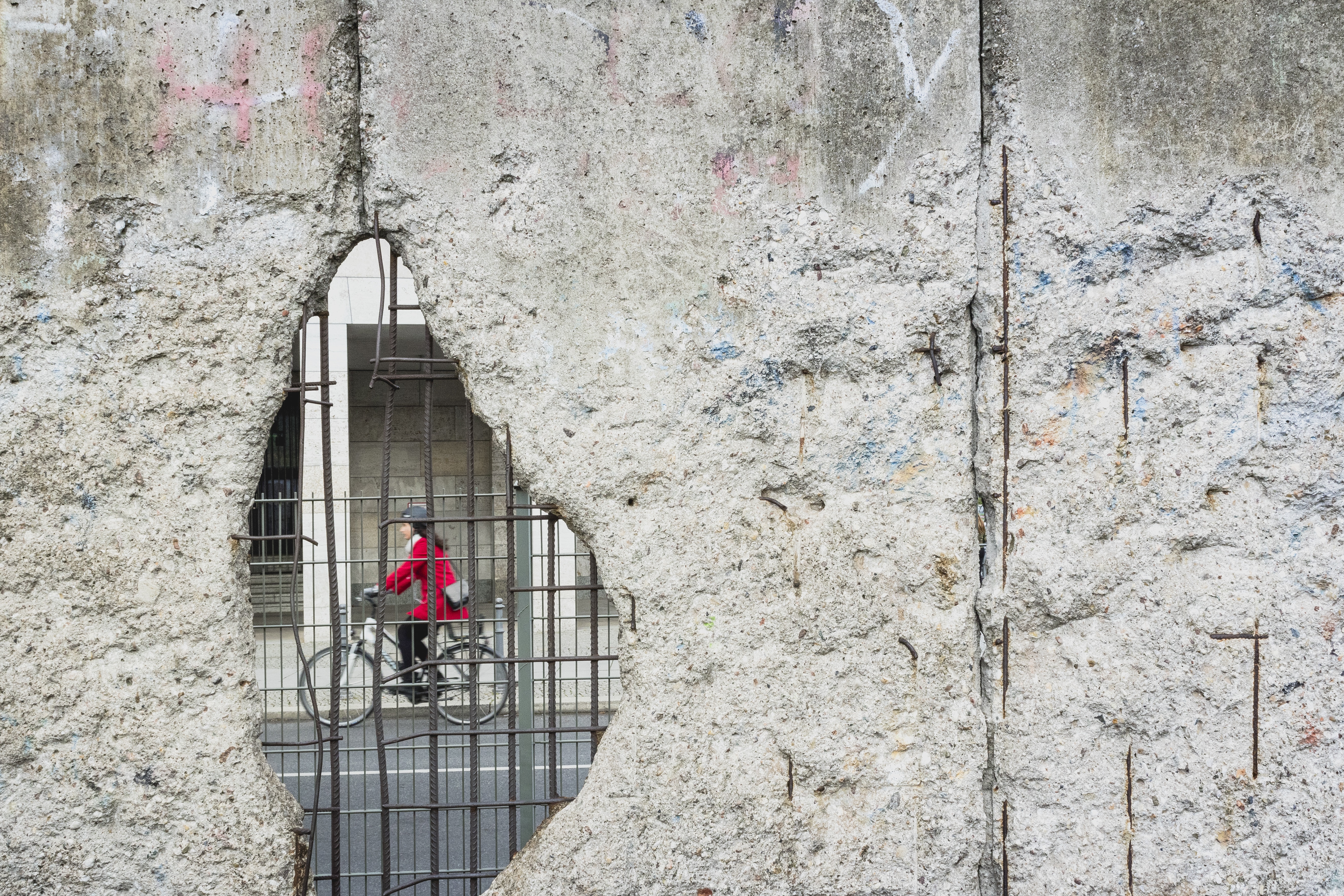 black haired female riding on bicycle seen through hole in gray concrete wall