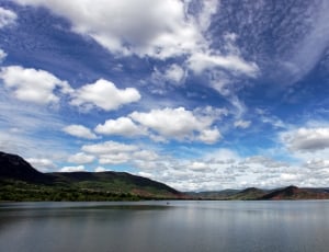 photo of body of water so rounded with mountains under calm sky during day time thumbnail