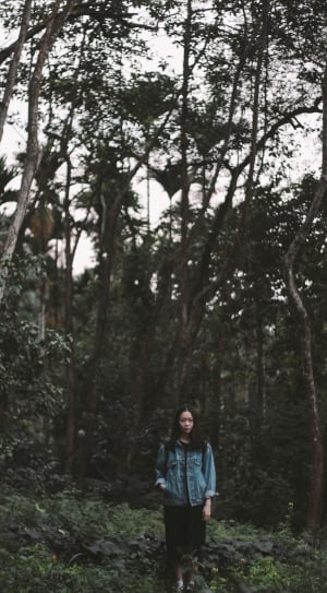 woman in blue denim long sleeve shirt standing outside surrounding trees at daytime thumbnail