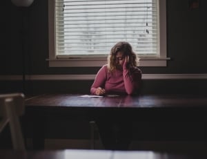 woman in pink sweater sitting beside brown wooden table during daytime holding her face thumbnail