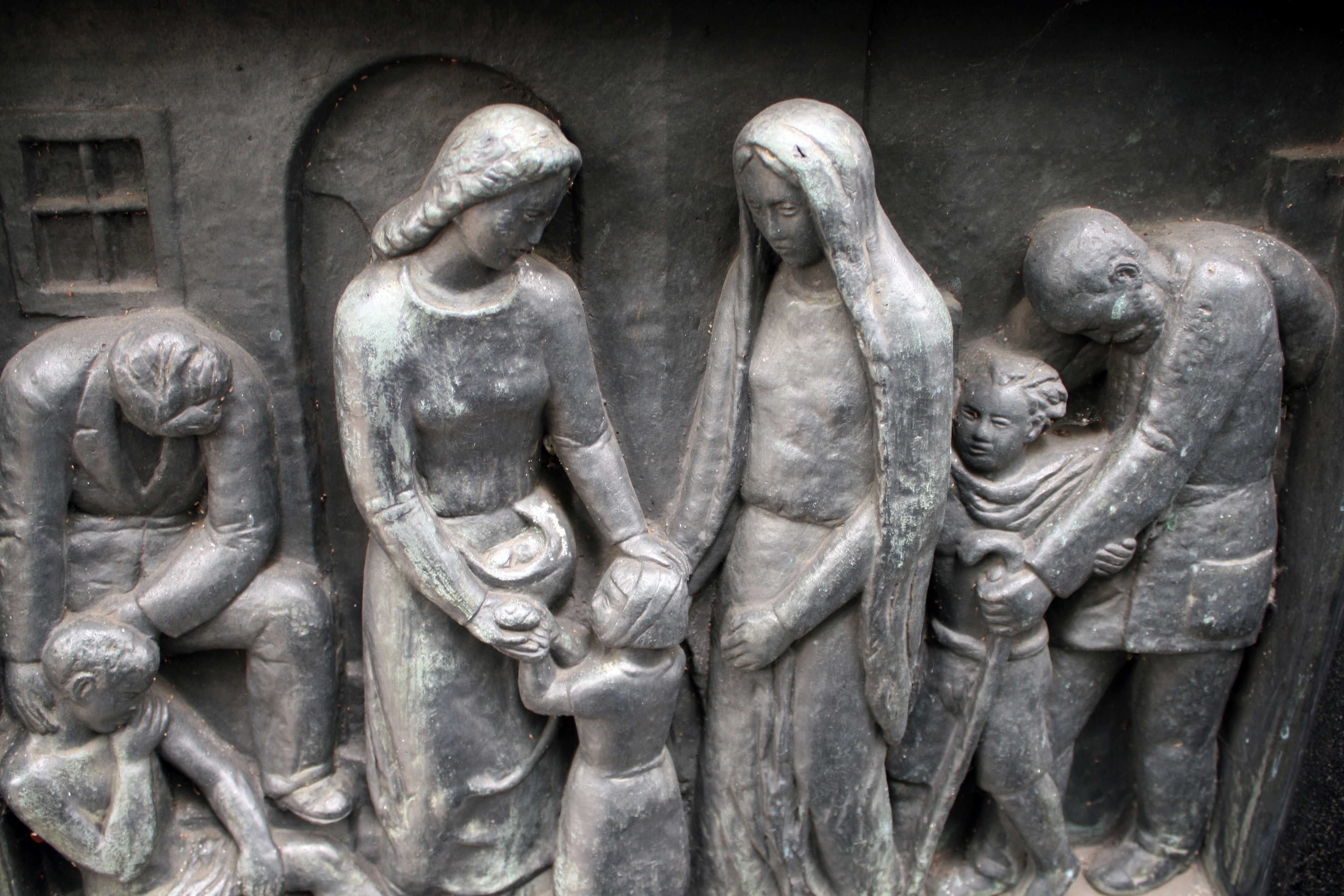 gray sculpture of 2 women tending to a girl