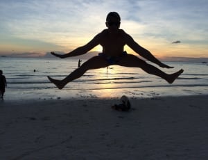 silhouette photo of jumping man near beach during golden hour thumbnail