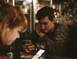 man in brown sweater sitting by the table near woman in red tops during nighttime thumbnail