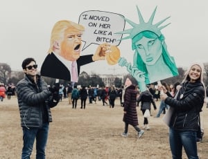 man and woman holding cutout of donald trump and statue of liberty during daytime thumbnail