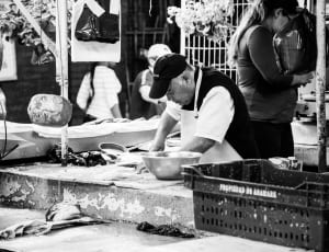 man selling fish in wet market grayscale photo thumbnail
