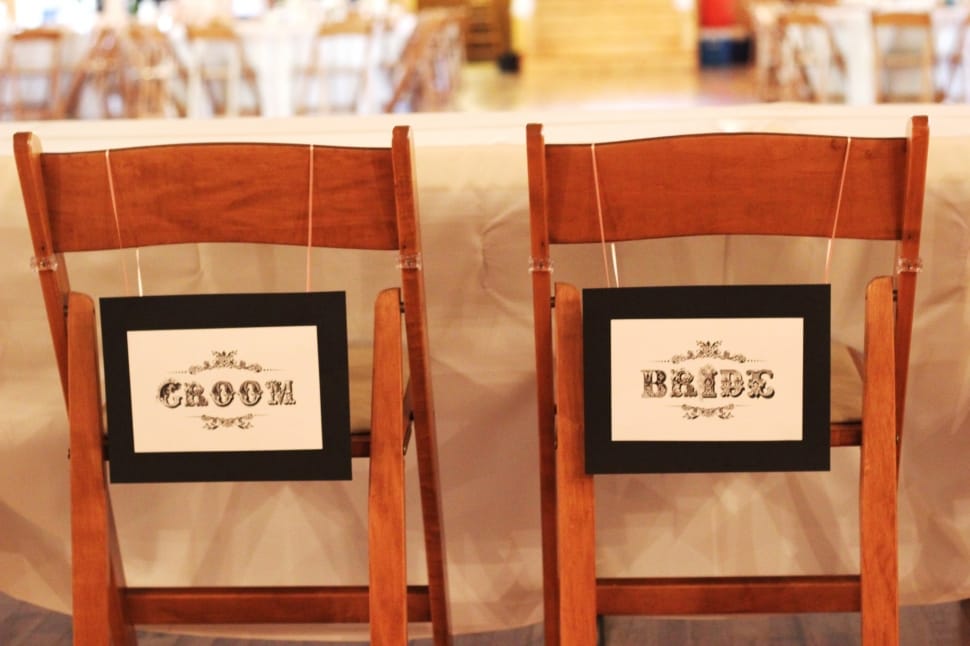 2 brown wooden chairs with groom and bride signage preview