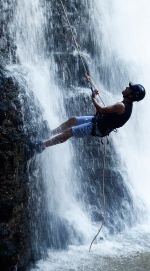 man in black tank top and blue short climbing near waterfalls thumbnail