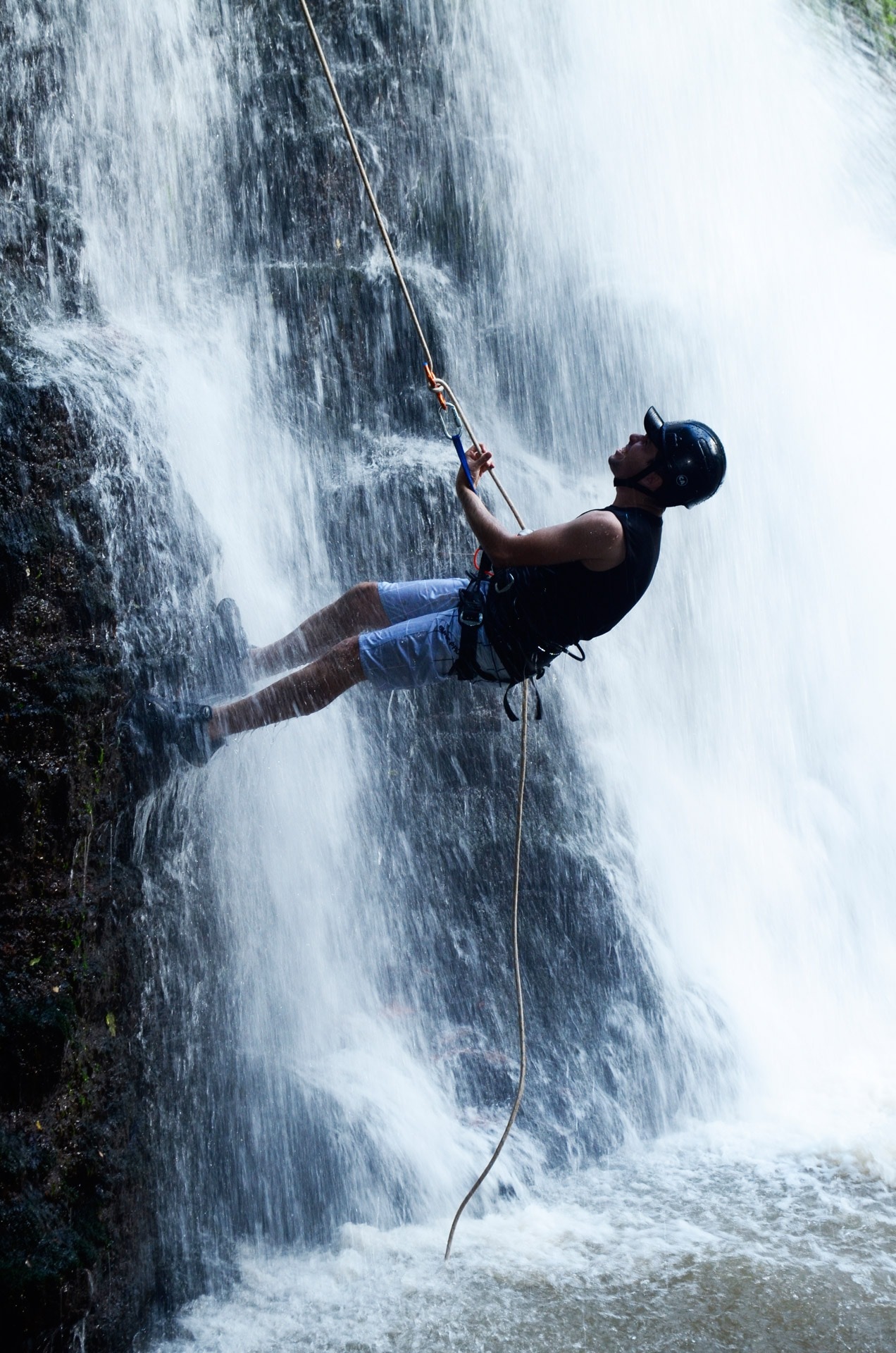 man in black tank top and blue short climbing near waterfalls