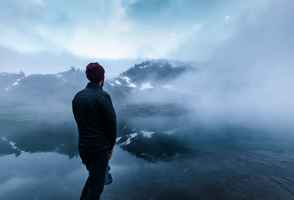 man wearing bubble jacket standing in front of body of water with fog preview