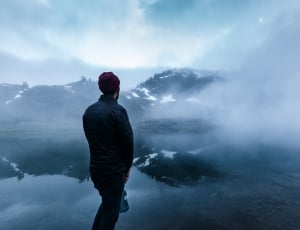 man wearing bubble jacket standing in front of body of water with fog thumbnail