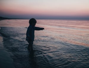 child standing on seashore during golden hour thumbnail