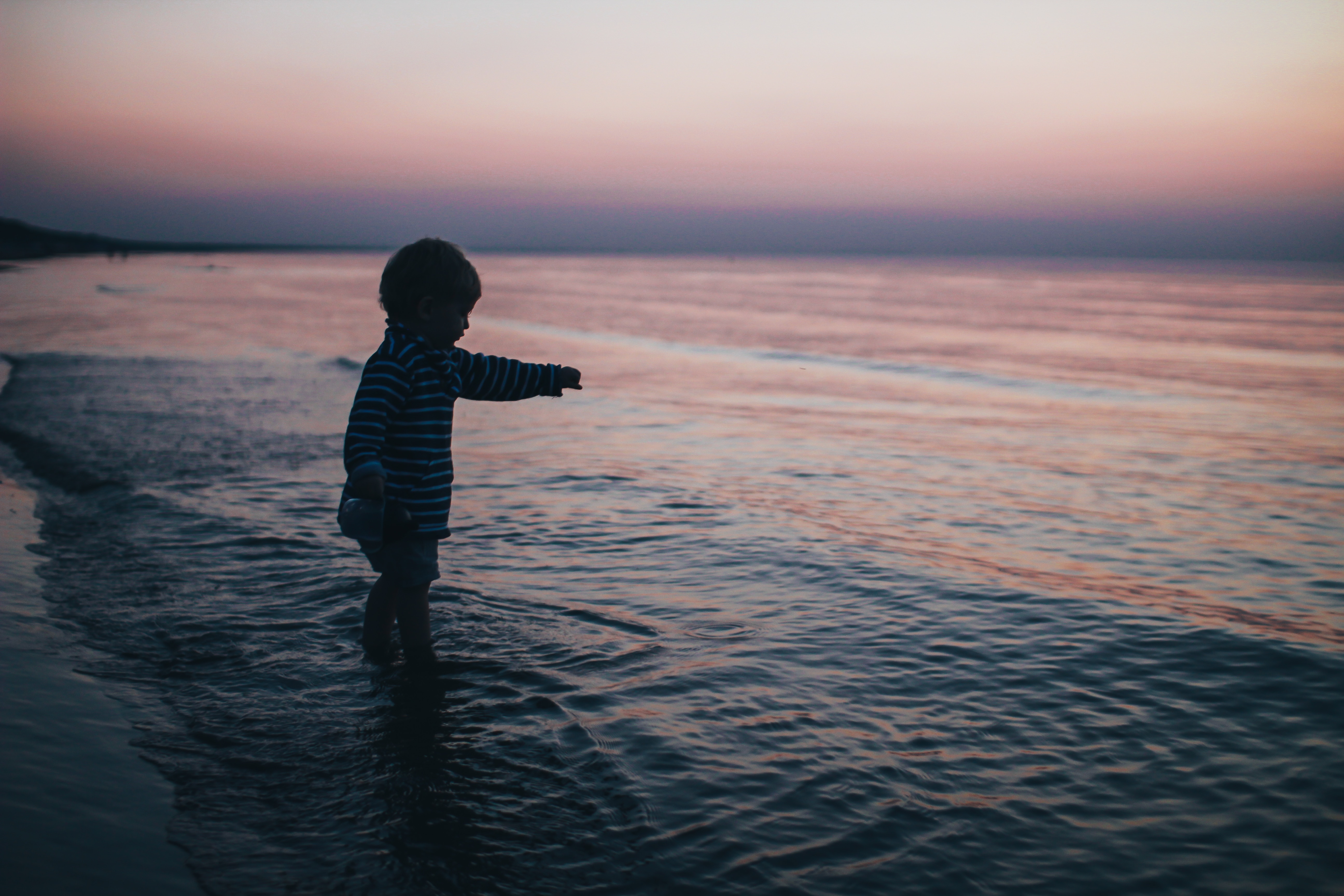 child standing on seashore during golden hour