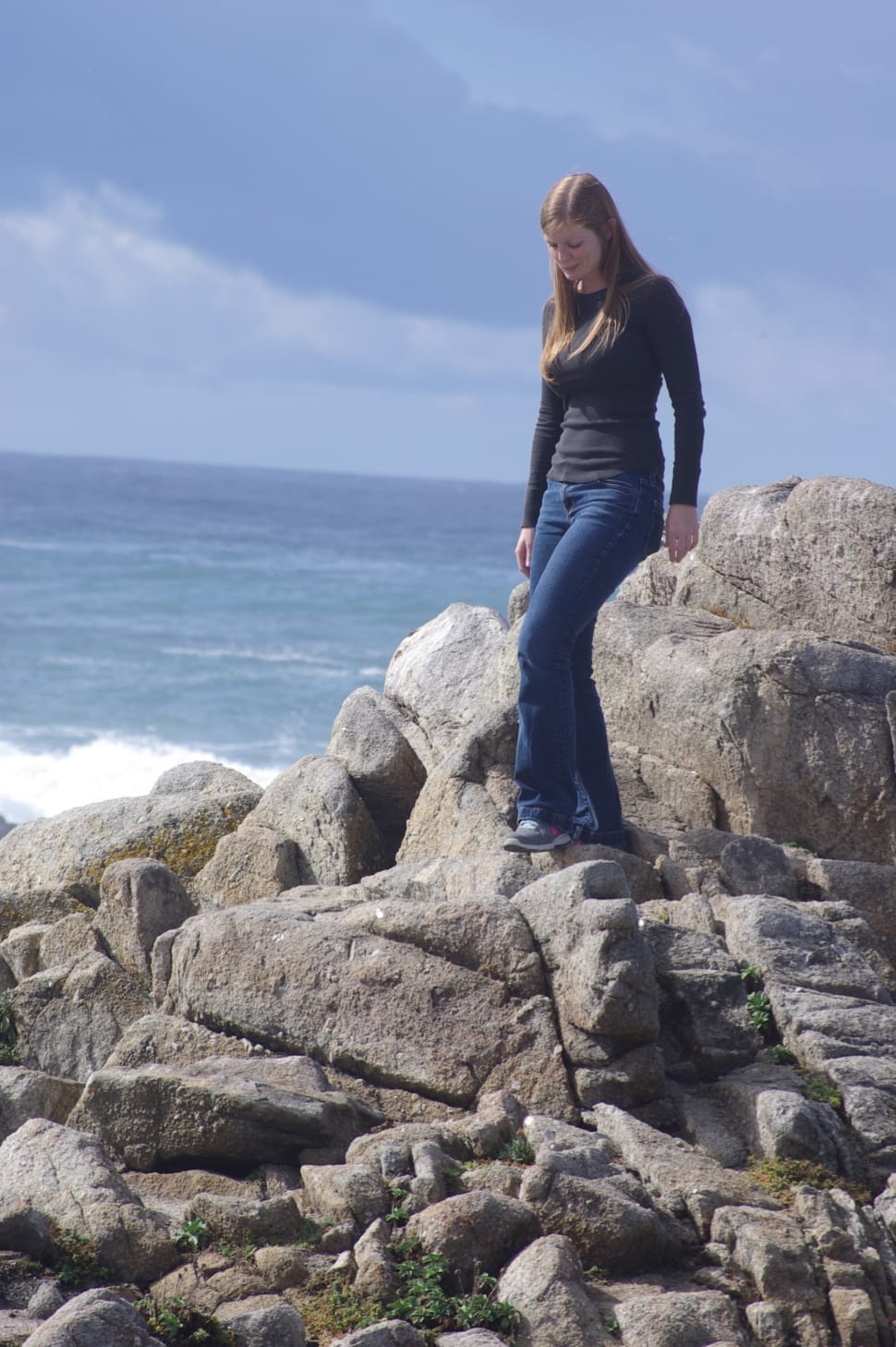 girl wearing black long sleeve and blue denim pants on side of body of water during day time preview
