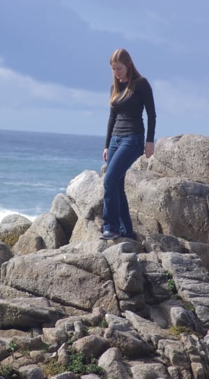 girl wearing black long sleeve and blue denim pants on side of body of water during day time thumbnail