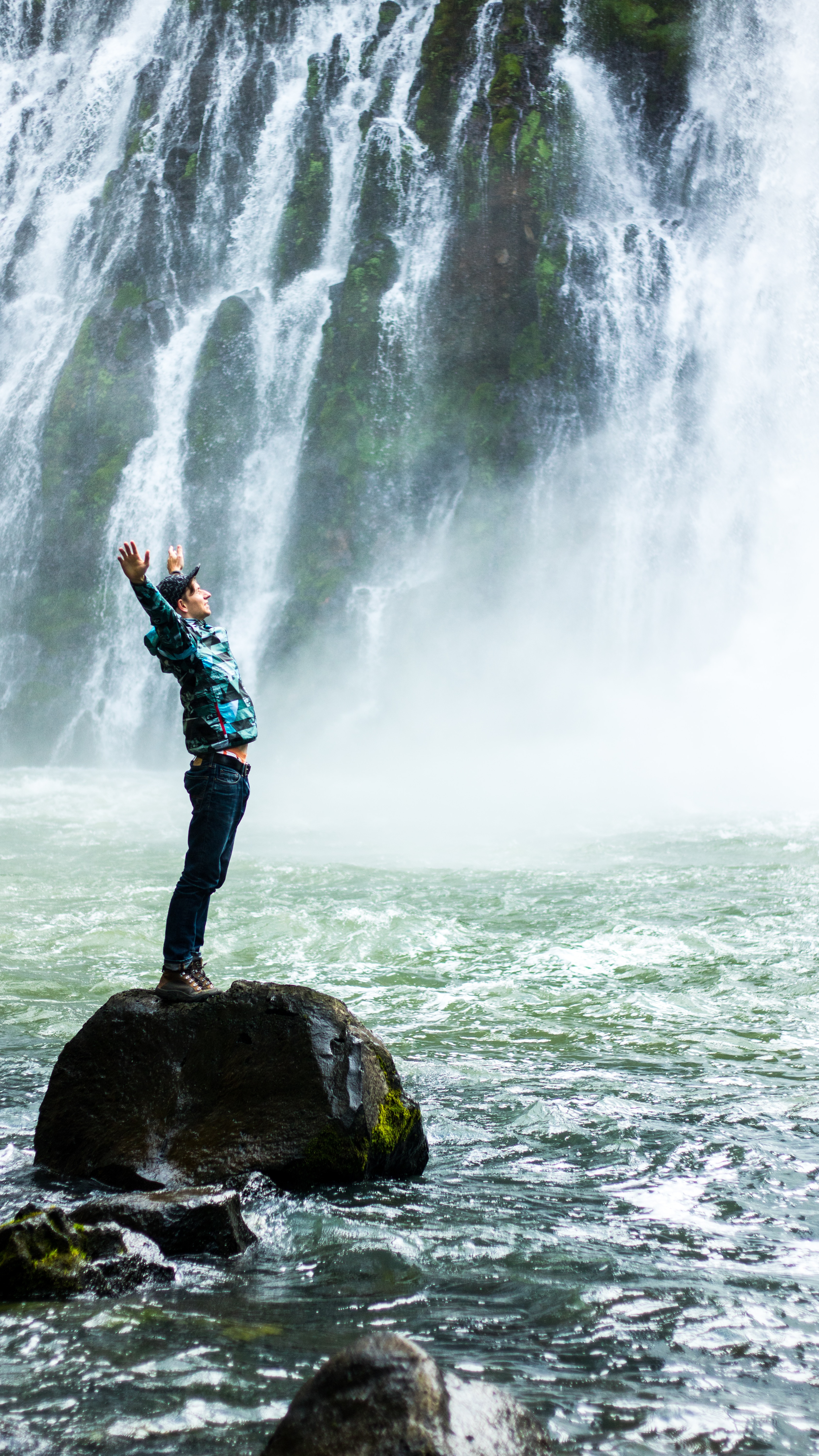 man stretching arms wide open standing on rock near waterfalls