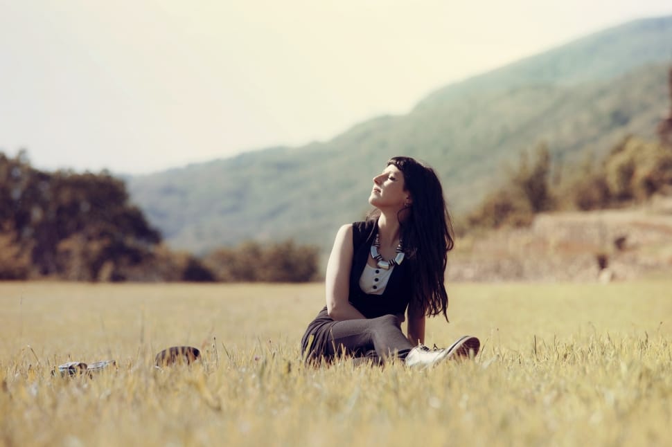 girl sitting on grass filed behind mountain hill preview