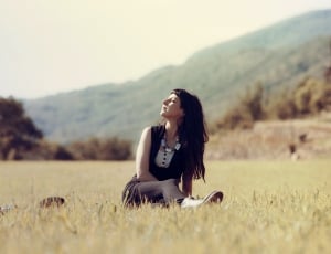 girl sitting on grass filed behind mountain hill thumbnail