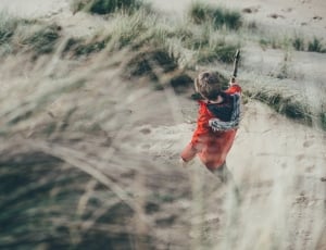 boy in red jacket standing near grasses thumbnail