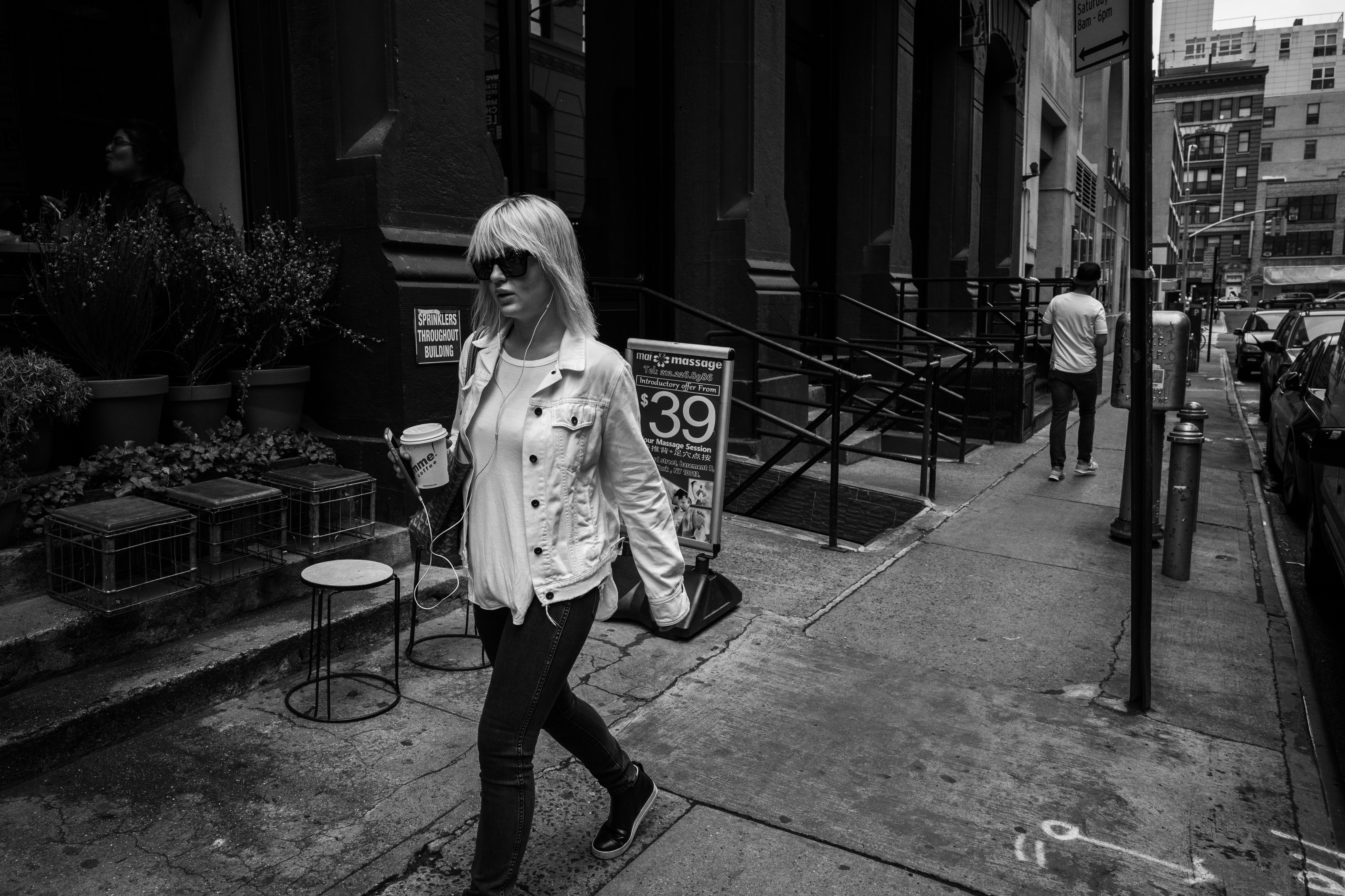 gray scale photo of woman walking on sidewalk near building