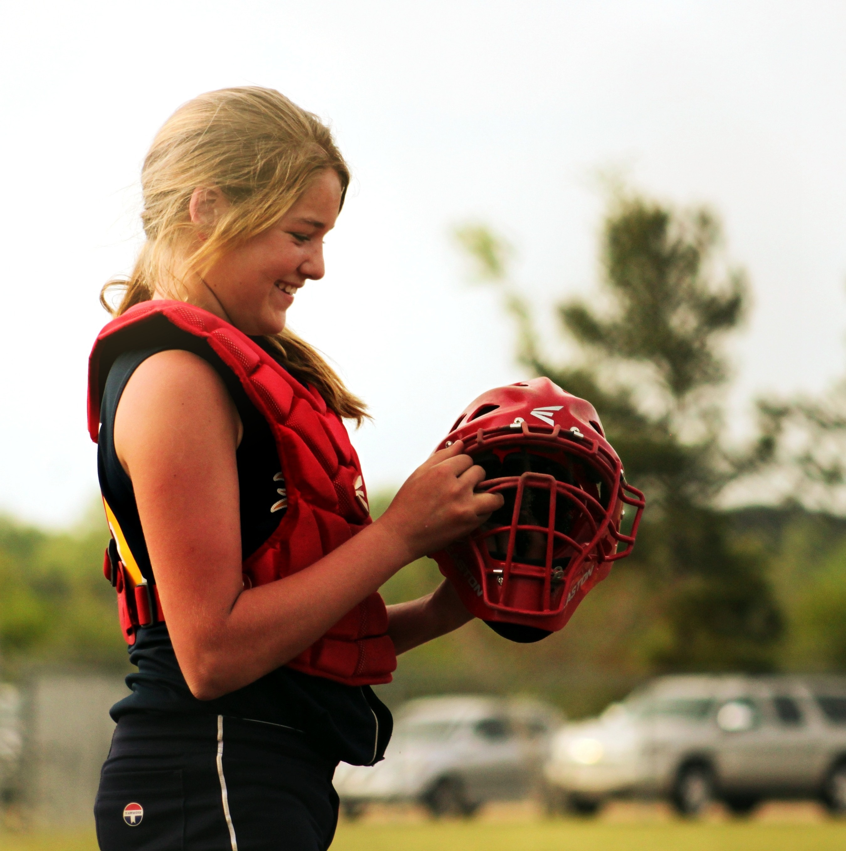 woman holding red softball catcher helmet