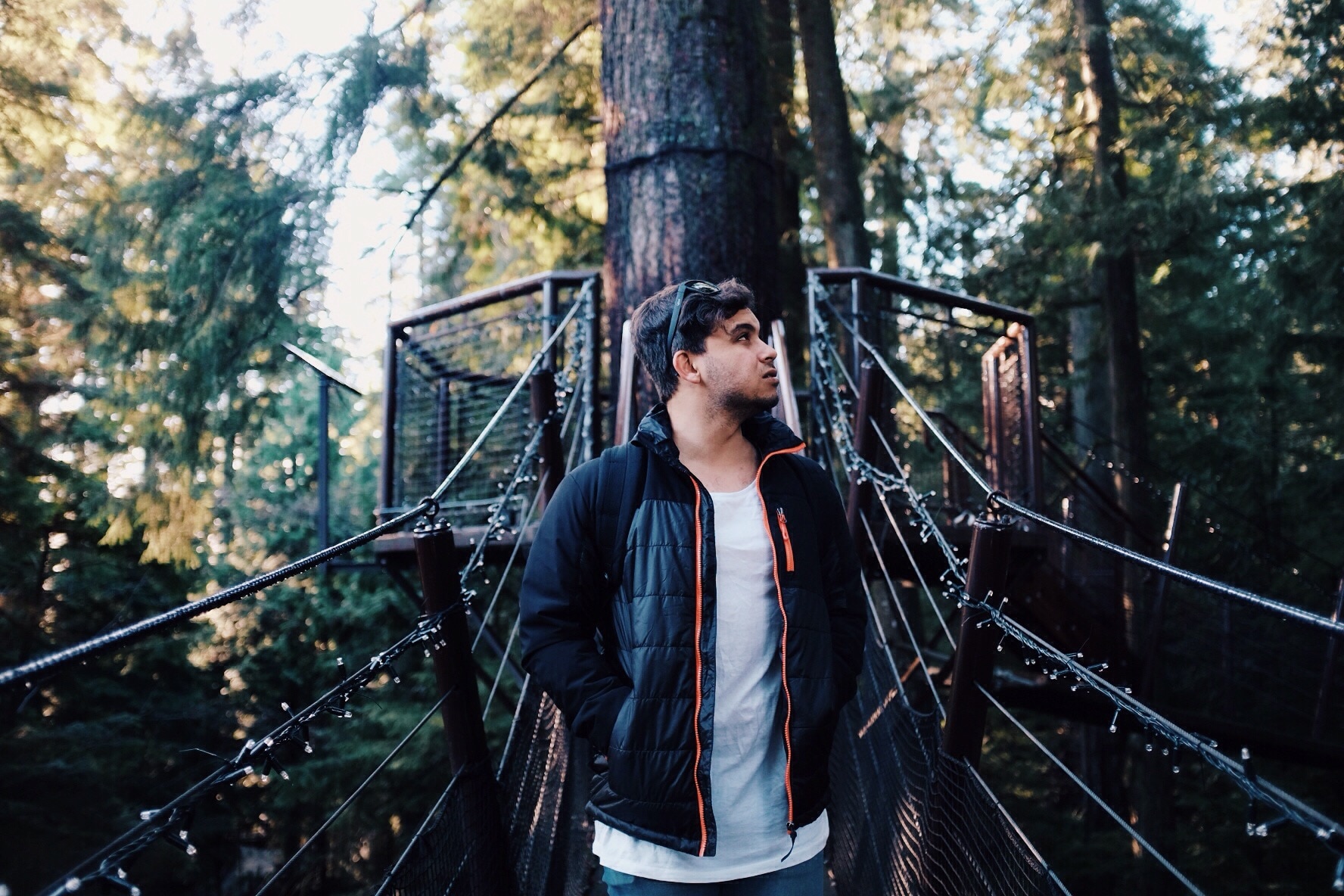 man in black zip-up jacket and white inner shirt on hanging bridge and tree bark view behind