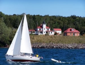 white sail ship on body of water near house thumbnail