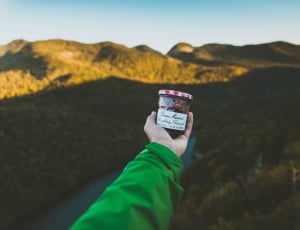 person holding a round container in front of green mountain during daytime thumbnail