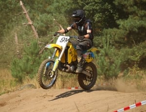 man riding yellow and white dirt bike performing motor cross during daytime thumbnail