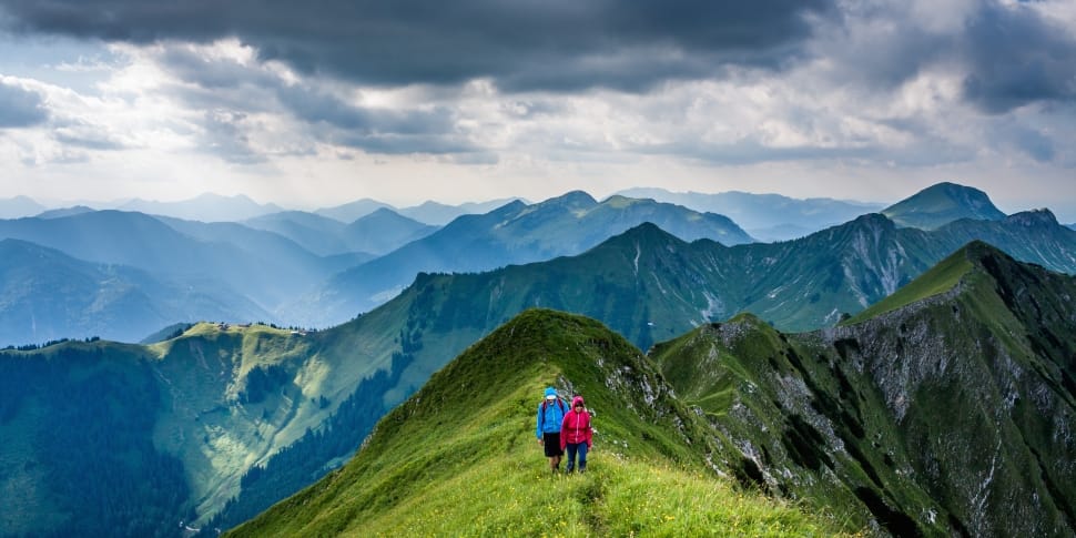 two people walking on mountain under gray sky during daytime preview