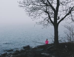 woman in pink jacket near body of water thumbnail