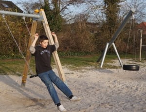 boy's brown crew neck shirt, blue jeans and white low top sneakers outfit riding a brown swing thumbnail