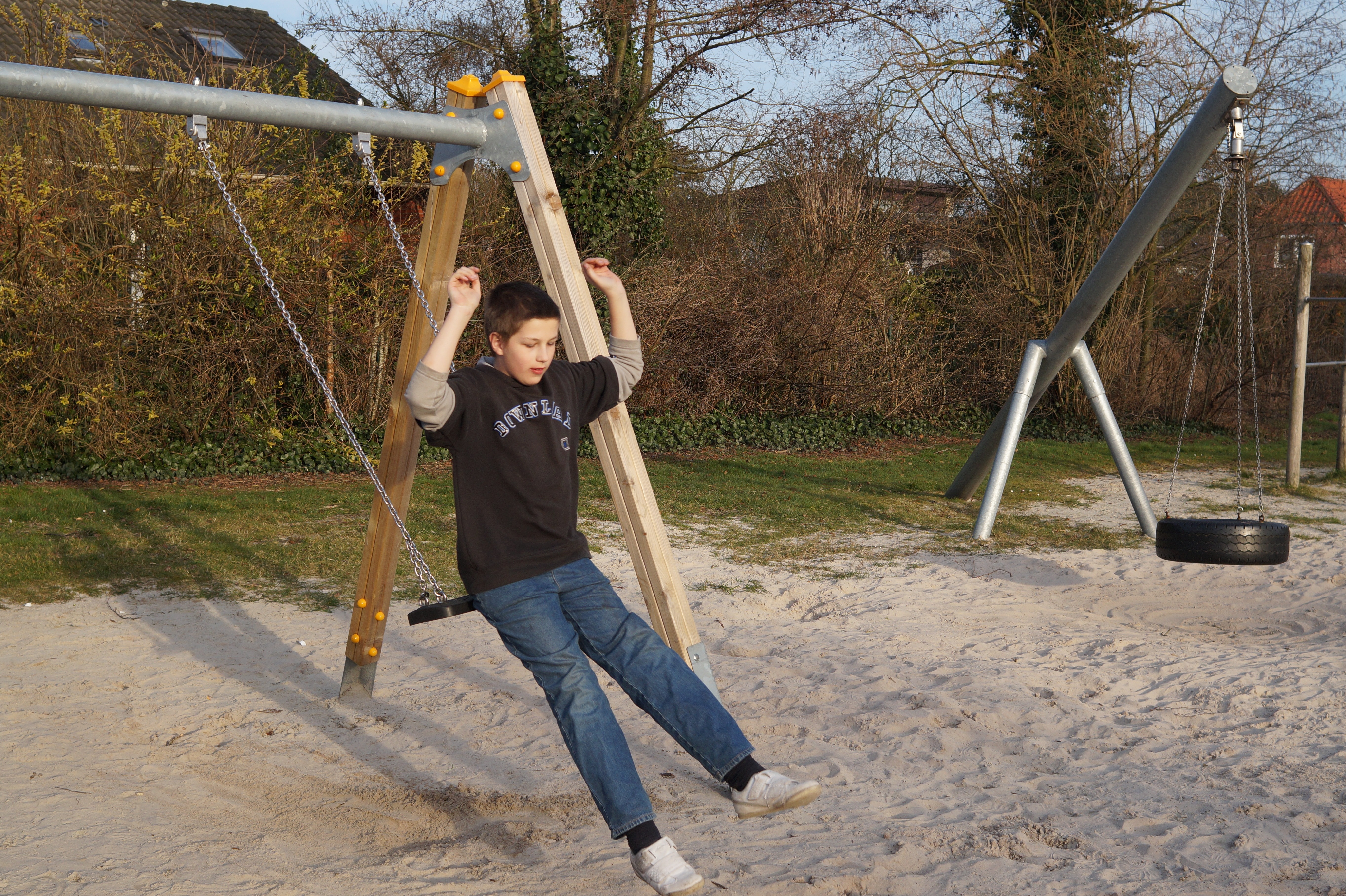 boy's brown crew neck shirt, blue jeans and white low top sneakers outfit riding a brown swing